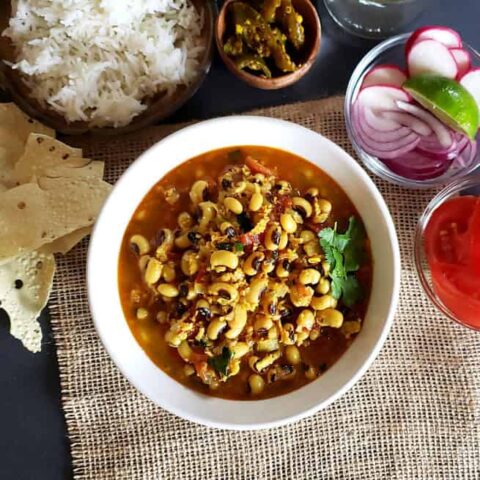 A dinner serving of creamy black-eyed peas and coconut curry with rice, pickle, papad and fresh onion tomato salad.