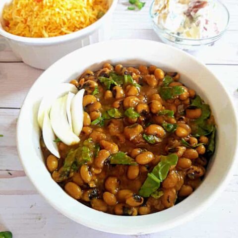 Black Eyed Peas cooked with onions, tomatoes and spinach with delicious seasoning served in white bowl.