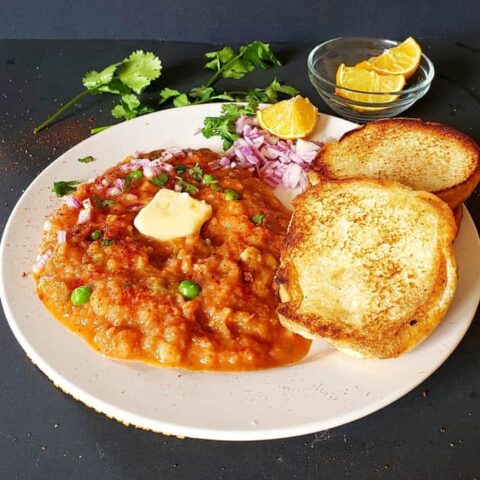 A white dinner plate with garnished spicy bhaji and buttery dinner rolls served along with lemon wedges and cilatrol leaves. This lip smacking delicious meal is easy to prepare in Instantpot.