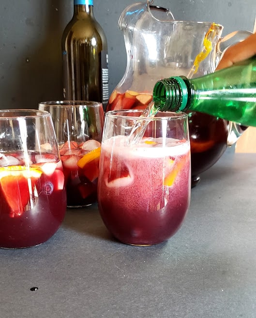 A process shot showing sparkling water getting poured in a glass of red sangria mix.