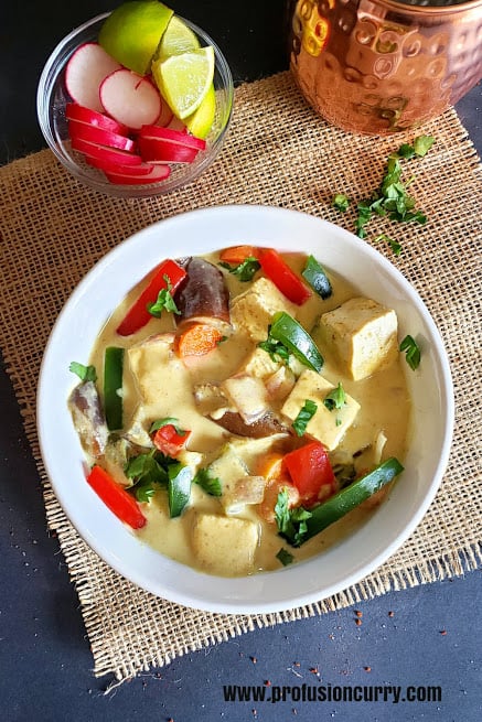 A white serving bowl full of tofu, vegetables in creamy coconut curry.