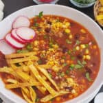 A bowl of vegetarian tortilla soup is served for dinner along with other garnishes.