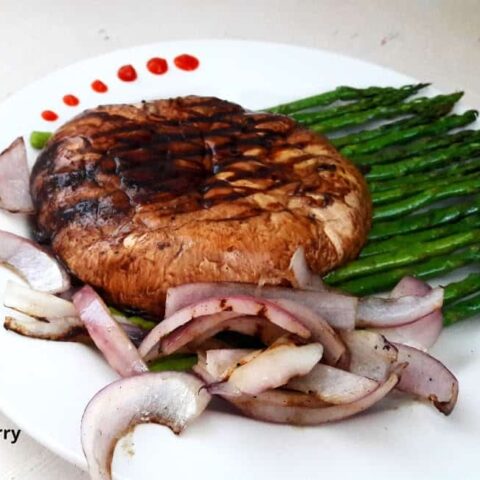 A dinner serving with grilled portbello mushrooms, asparagus and onions.