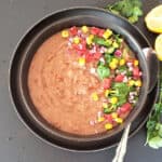 Homemade refried pinto beans served in a dinner bowl along with garnishes.