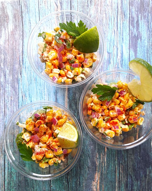 Mexican Corn Salad with corn, cheese, mayo and spices served in a cup with lemon wedges