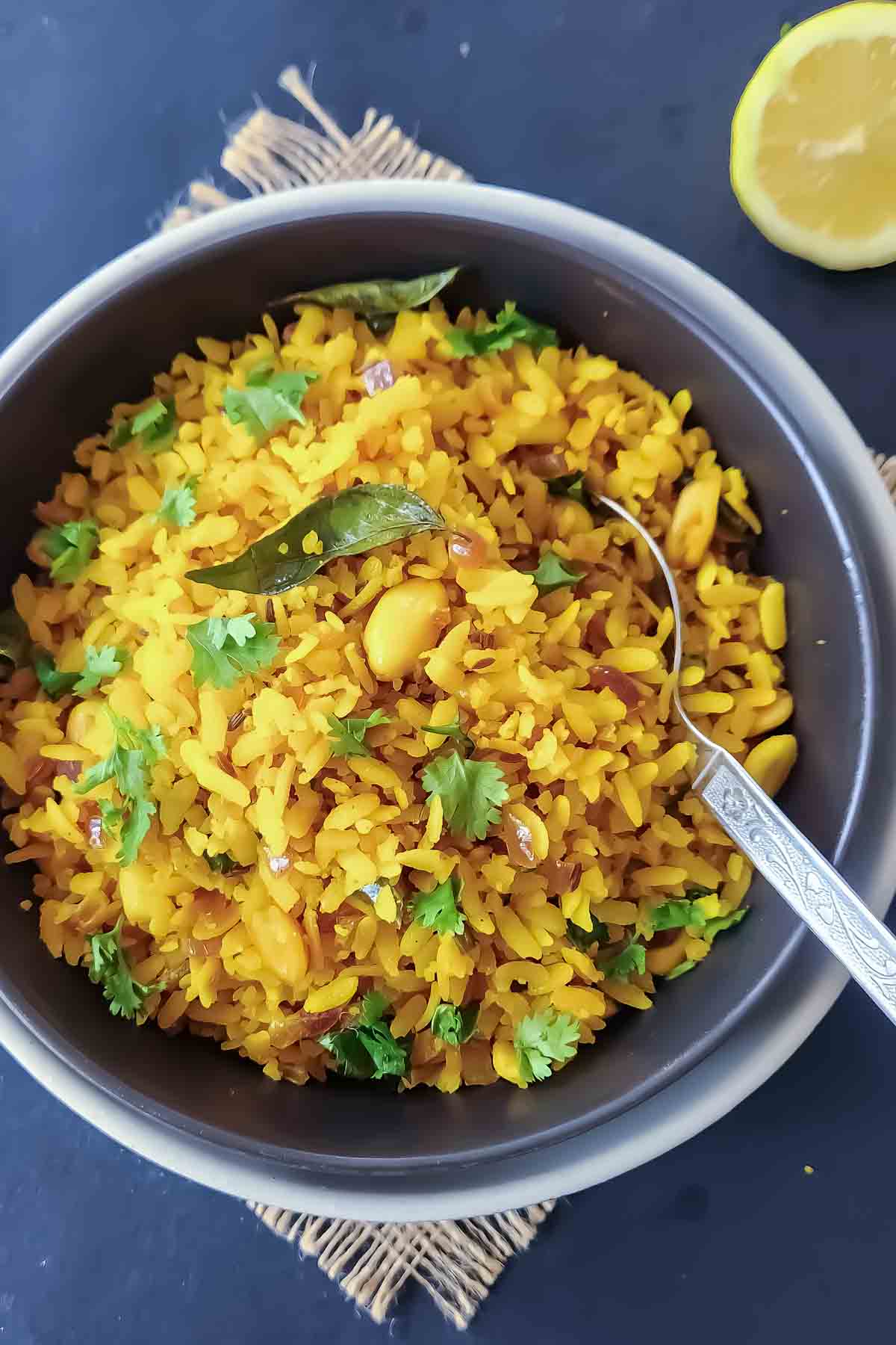 Bowl of traditional Poha topped with peanuts, cilantro, and fresh lemon wedges.