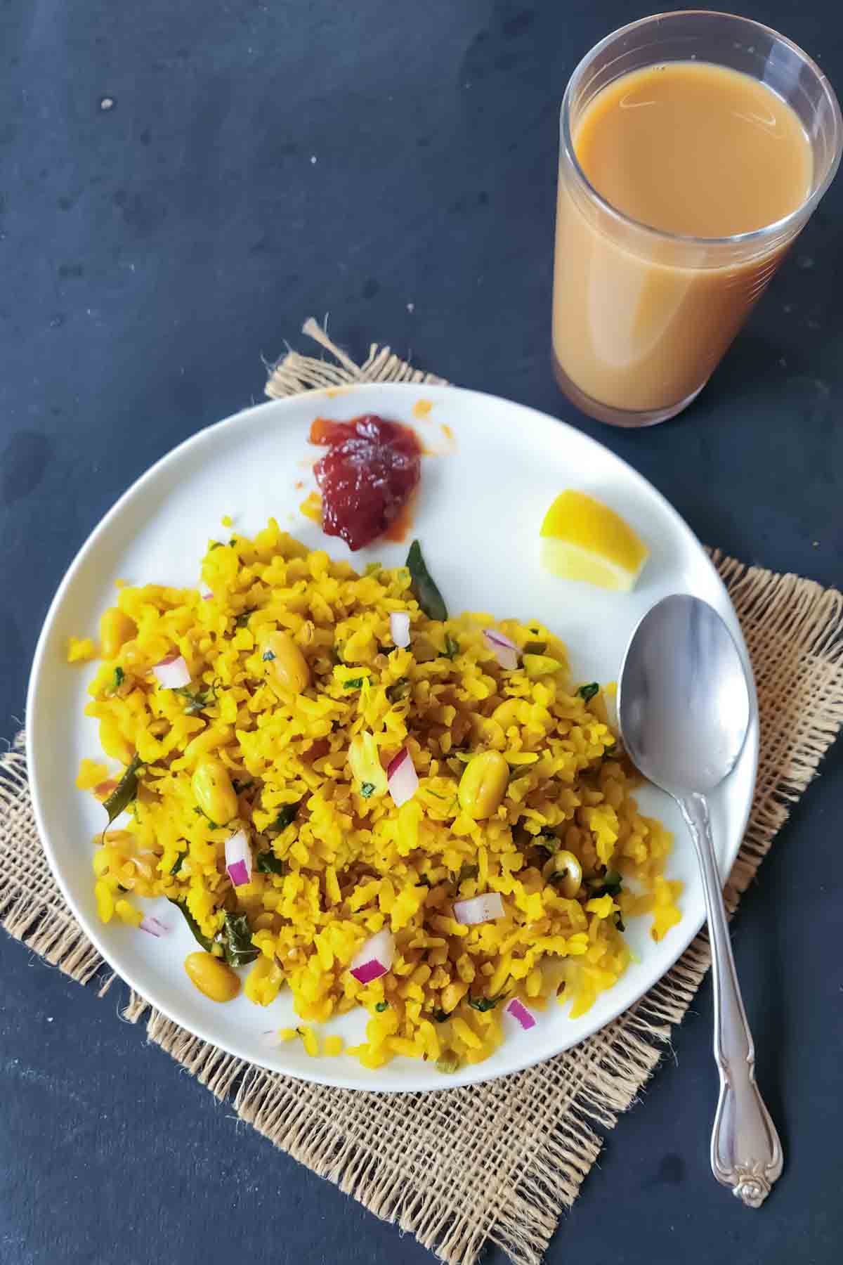 Vegan Kanda Poha served in a white bowl with roasted peanuts and fresh herbs with a side of masala chai and pickle.