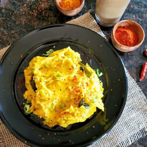Yellow spicy Tandalachi Ukad is rice flour roux served on a black dinner plate along with ginger masala chai.