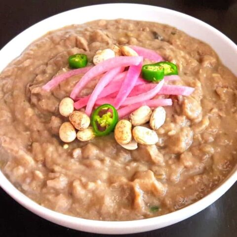 Pinto Beans served as mexican style refried beans in white bowl and garnished with pickled onion and jalapeno pepper slices