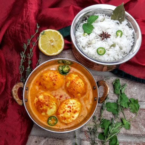 An over head shot of Indian Egg curry and white rice served in copper containers.