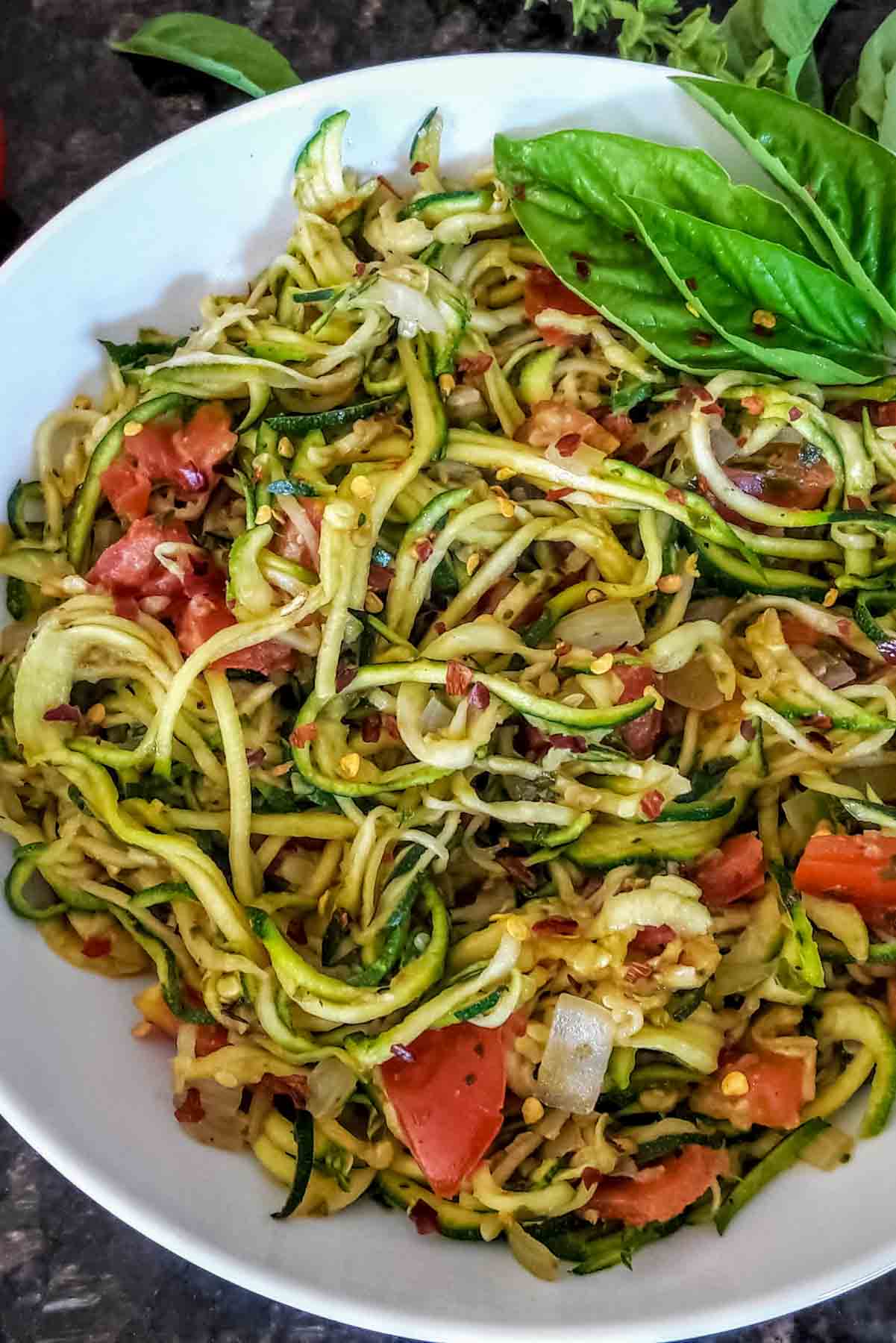 Zoodles, or spiralized zucchini, tossed with Italian seasoning and other veggies to make a fantastic gluten-free pasta substitute.
