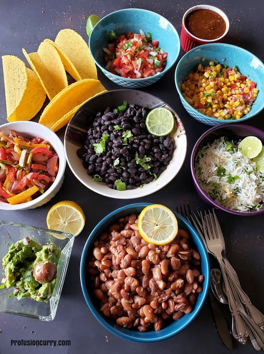 Colorful bowls full of beans, rice and condiments set up for make your own taco bar.