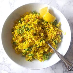 Turmeric Lemon rice served in a white bowl along with lemon wedges and chopped cilantro and green pepper.