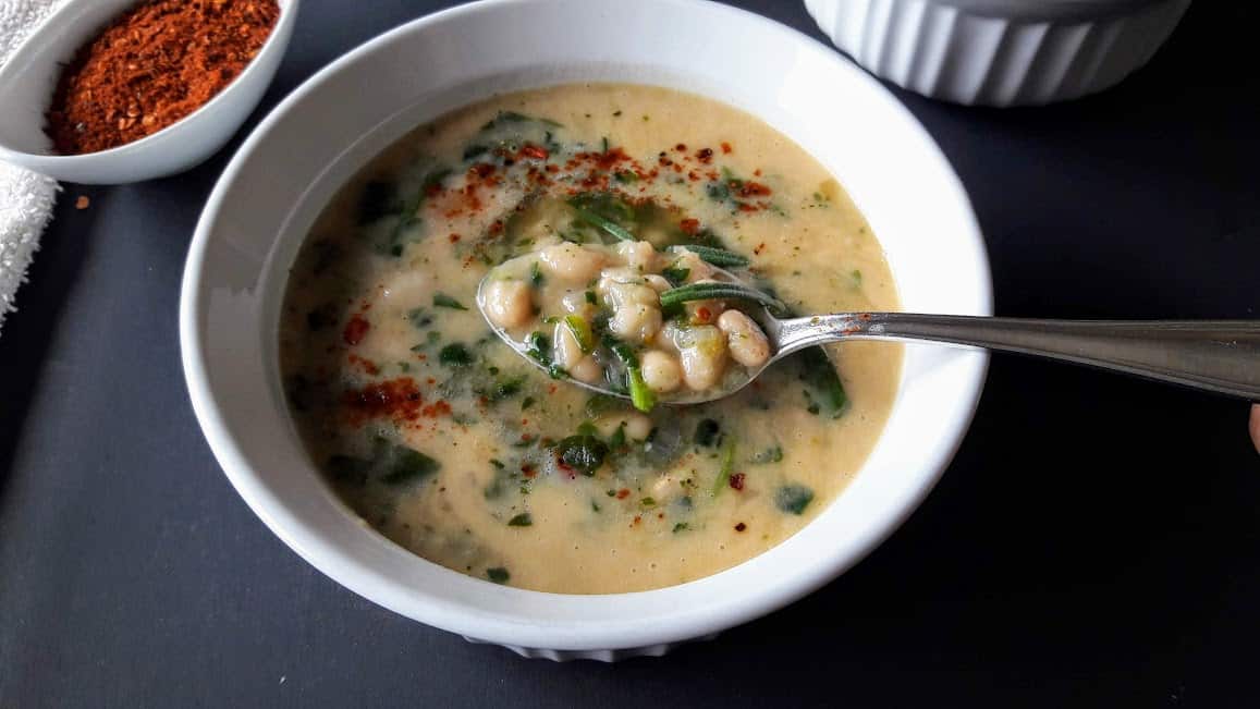 A spoon full of seasoned white beans in creamy soup.