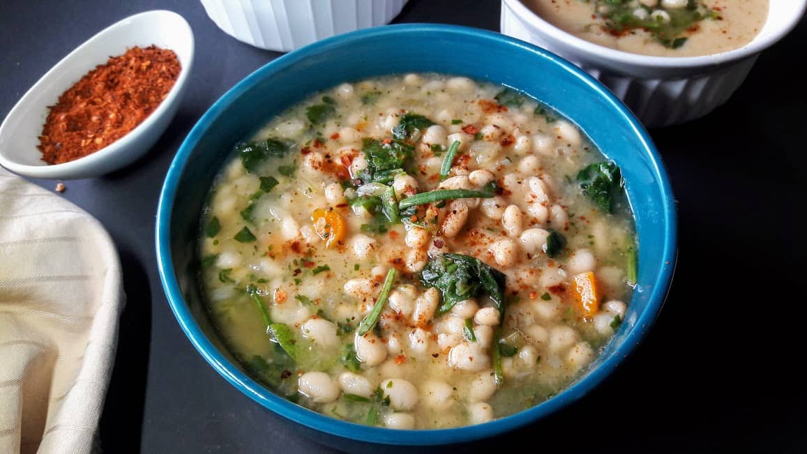A blue bowl full of vegan White Bean and Spinach Soup made in Instant Pot.