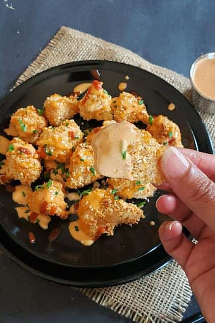 A cauliflower wing dipped in spicy, creamy bang bang sauce.