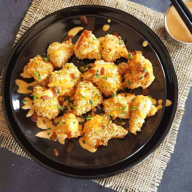 Crispy non fried cauliflower bites tossed with spicy, creamy bang bang sauce served on a black dinner plate.