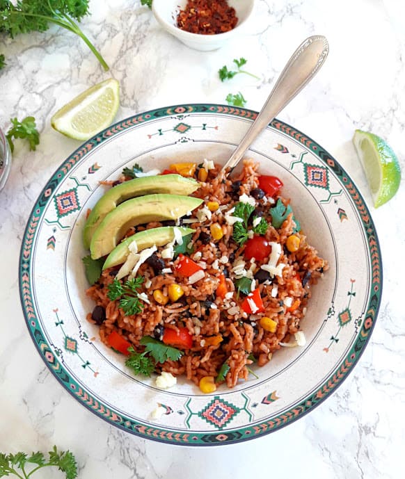 Vegan enchilada rice with garnishes and lime wedges overhead shot