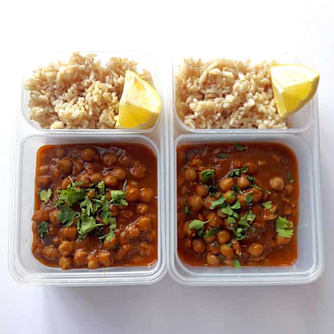 Chole with brown rice in two lunch containers with lemon wedges