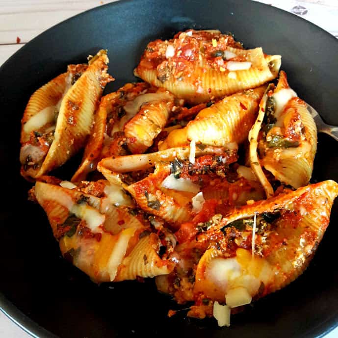 Overhead shot of Stuffed Shells filled with spinach, cheese and Italian Seasoning. Pefect weeknight comforting dinner served on black plate with cheese sprinkled on top.