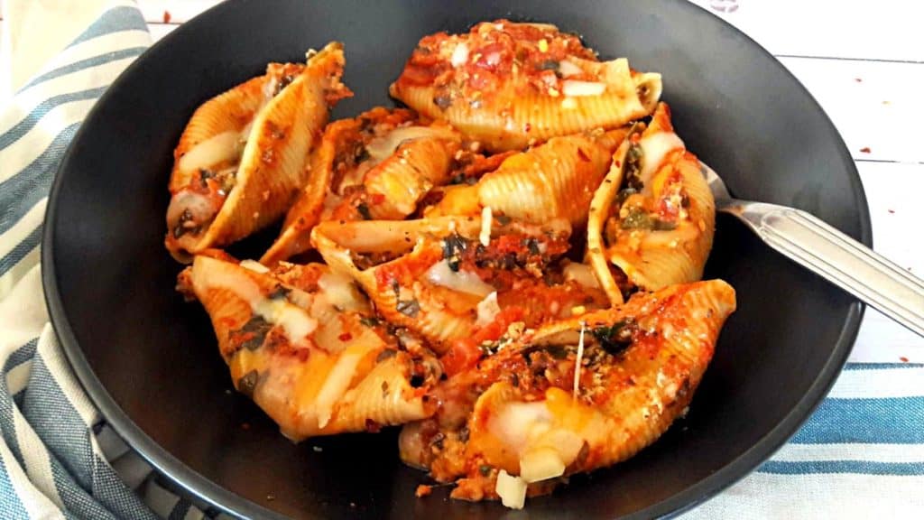 Jumbo Pasta Shells filled with spinach, cheese and Italian Seasoning. Pefect weeknight comforting dinner served on black plate with cheese sprinkled on top.