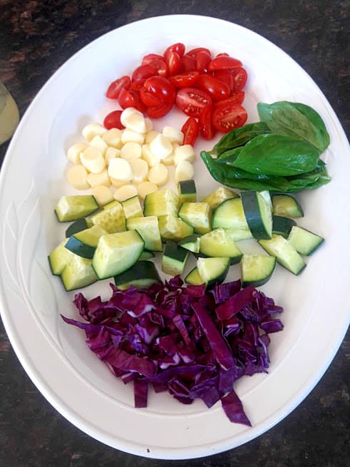 Italian Summer pasta salad with colorful veggies cherry tomatoes, crisp cucumbers, purple cabbage. It also includes zesty dressing and fresh aromatic basil