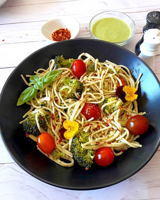 Spaghetti with broccoli and cherry tomatoes with fresh basil, chili flakes on black serving plate with creamy lemon dressing on the side. A delicious ProfusionCurry recipe