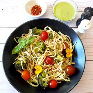 Spaghetti with broccoli and cherry tomatoes with fresh basil, chili flakes on black serving plate with creamy lemon dressing on the side. A delicious ProfusionCurry recipe