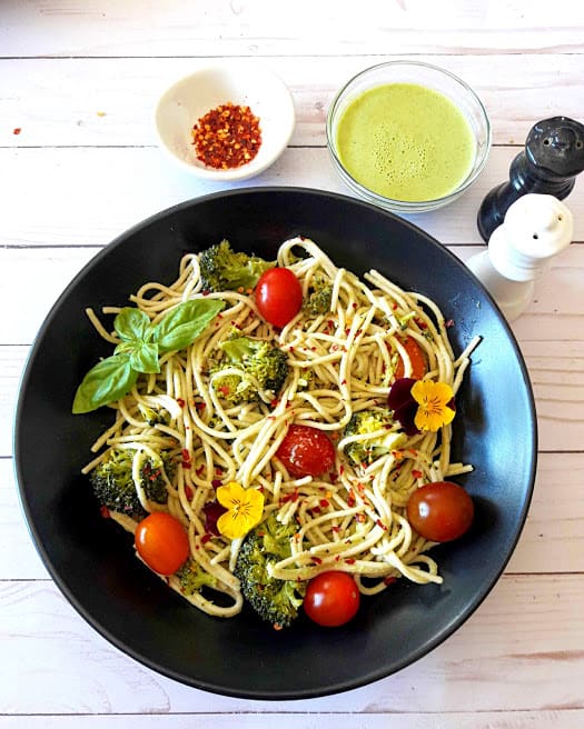 Spaghetti with broccoli and cherry tomatoes with fresh basil, chili flakes on black serving plate with creamy lemon dressing on the side. A delicious ProfusionCurry recipe
