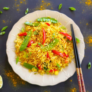 Golden turmeric hued Curry Fried rice served with colorful veggies on black background and chopsticks with lime wedges