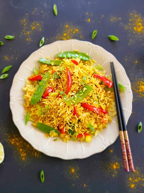 Golden turmeric hued Curry Fried rice served with colorful veggies on black background and chopsticks with lime wedges