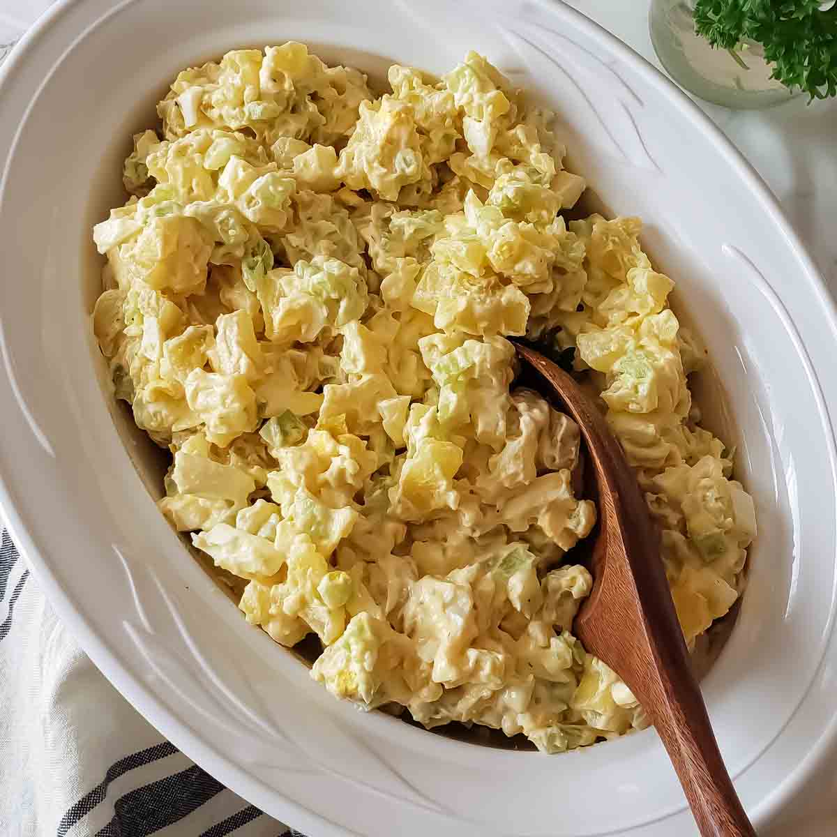 A large serving bowl with spoon full of classic potato salad with creamy dressing. This summer favorite recipe is perfect  for BBQ, picnics and potlucks.