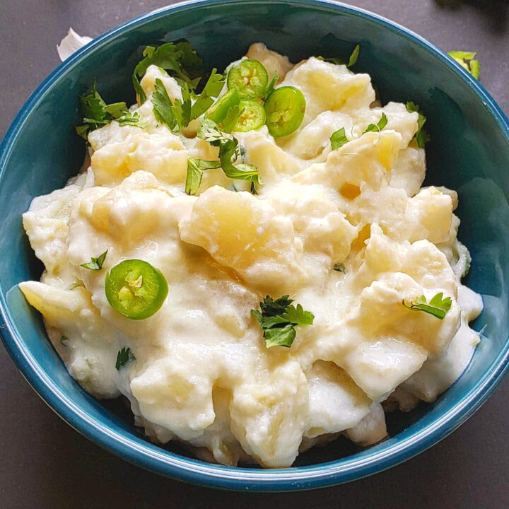 close up shot of Potato Salad coated with yogurt and garnished with cilantro and jalapeno peppers is served in blue bowl