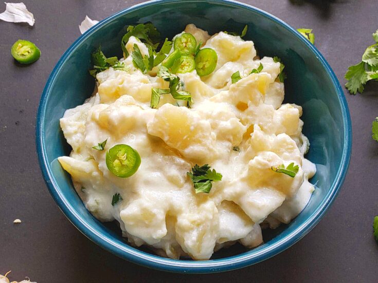 close up shot of Potato Salad coated with yogurt and garnished with cilantro and jalapeno peppers is served in blue bowl