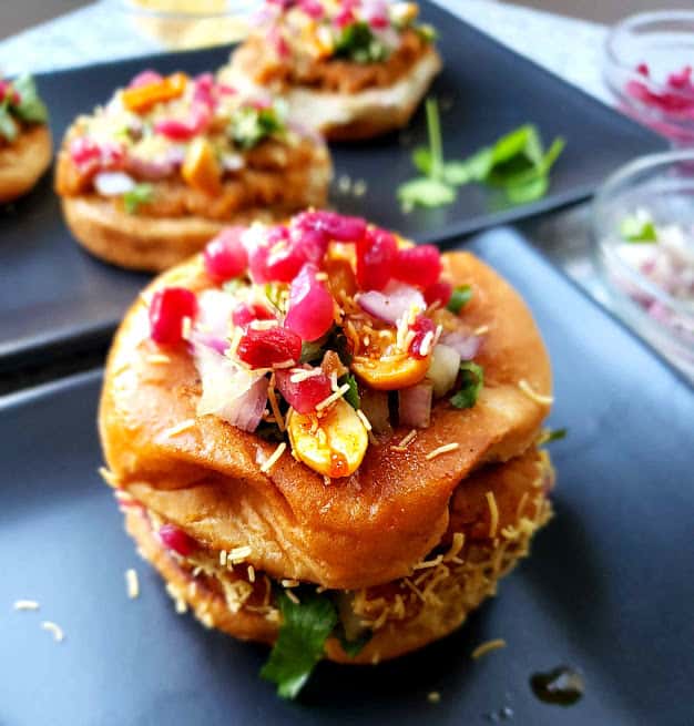 Dabeli, the popular Indian street food served on black plate with garnishes. 