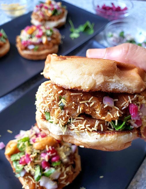 Close up shot of prepared Dabeli, Indian version of potato slider showing layers of garnishes and texture.