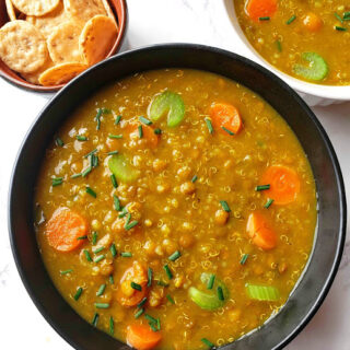 Lentil Quinoa Soup served in a black serving bowl garnished with fresh herbs .