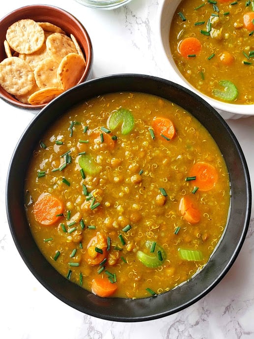 Lentil Quinoa Soup served in a black serving bowl garnished with fresh herbs .