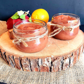 Two glass bottles of caramel color apple butter sauce displayed on wooden plank.