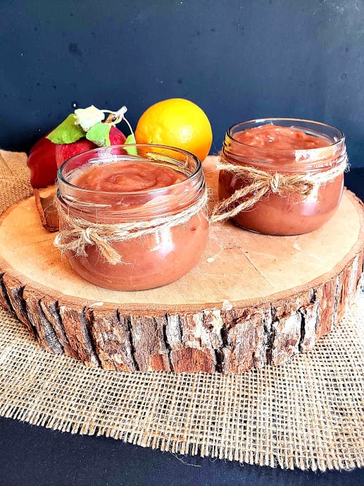 Two glass bottles of caramel color apple butter sauce displayed on wooden plank.