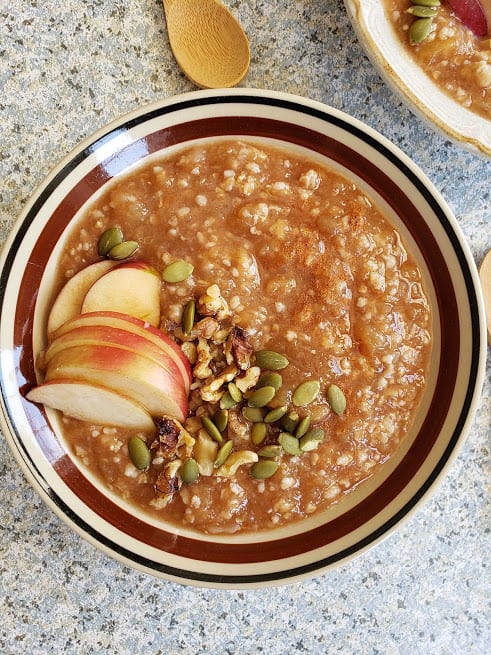 Apple cinnamon oats made in Instantpot served in brown bowl and garnished with apple slices and pumpkin seeds and walnuts. This creamy oatmeal is like eating dessert for breakfast.