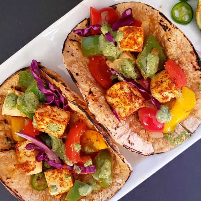 Paneer Fajita Tacos served with green sauce on white plate. This colorful recipe combines Indian Paneer with Mexican Taco seasoning making a lovely fusion.