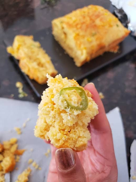 Holding a piece of homemade cornbread to show moist and slightly crumbly texture.