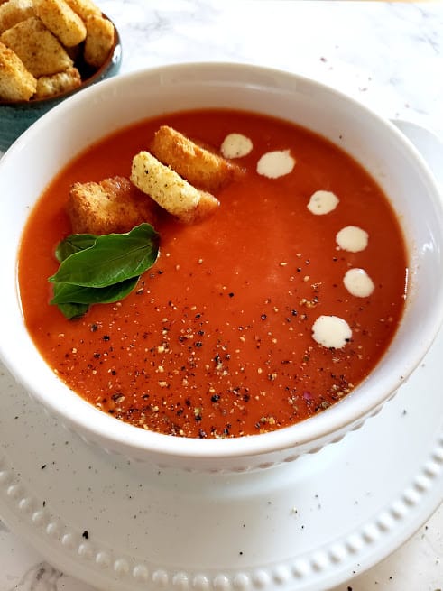 Close up photo of creamy and thick tomato bisque with cream, crutons. black pepper and basil garnish