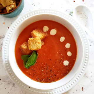 Thick and Creamy Vegan Tomato Bisque served in white bowl with garlic crutons, basil leaves and coconut cream garnish.