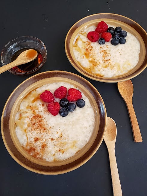 Klasszikus pudingszerű Tápióka puding két tálban, juharral és fahéjjal leöntve, friss bogyós gyümölcsökkel. Ez a profusioncurry recept vegán és gluténmentes és tojásmentes.