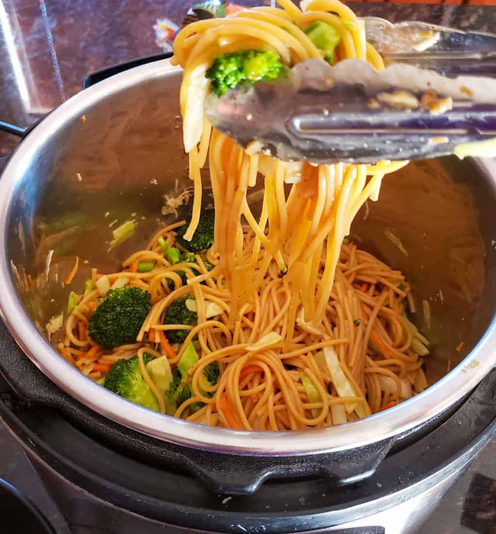 A tong lifting the seasoned noodles from Instant Pot.