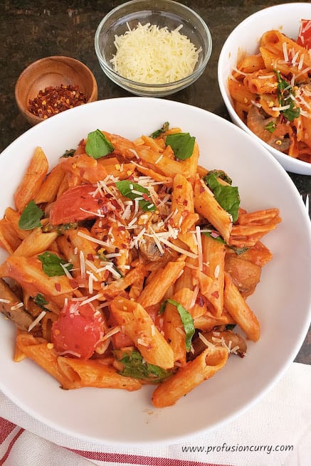 Delicious pasta in tomato cream sauce served in white dinner plate with parmesan cheese and red pepper flakes garnish. This instantpot pasta is ideal 20 minute weeknight dinner recipe.