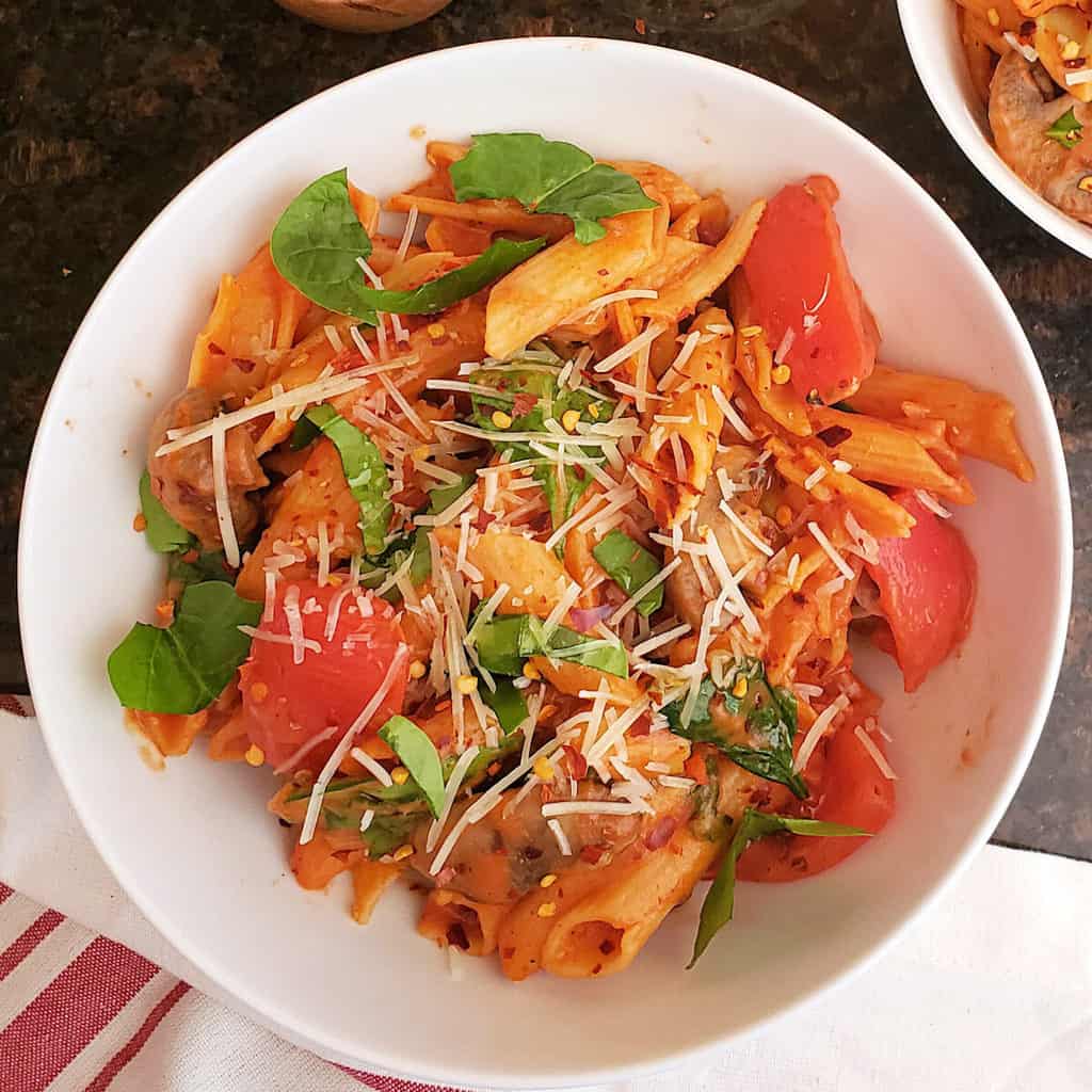 An Italian dinner pasta with tomato cream sauce served with tomatoes and spinach.