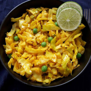 Turmeric Cabbage and peas stir-fry served in a bowl with two lime wedges for garnish.